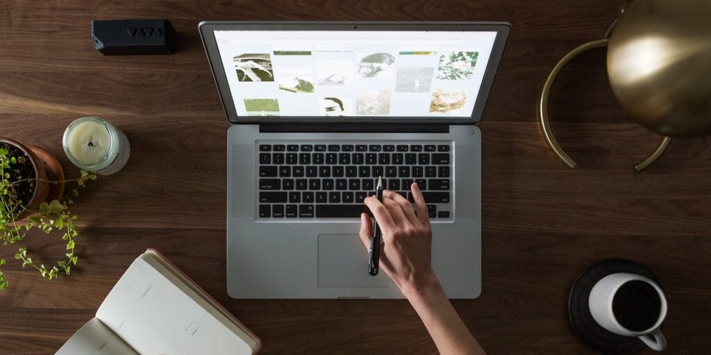 Plan vers le haut d'une personne qui utilise son ordinateur portable à un bureau avec un cahier et un café.
