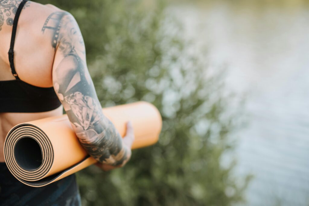 Personne tatouée qui tient un tapis de yoga dans sa mains. Plan rapprocher sur bras personne.