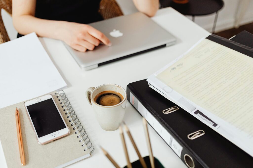 Bureau avec ordinateurs,café et matériel scolaire. Il y a une personne de l'autre côté du bureau