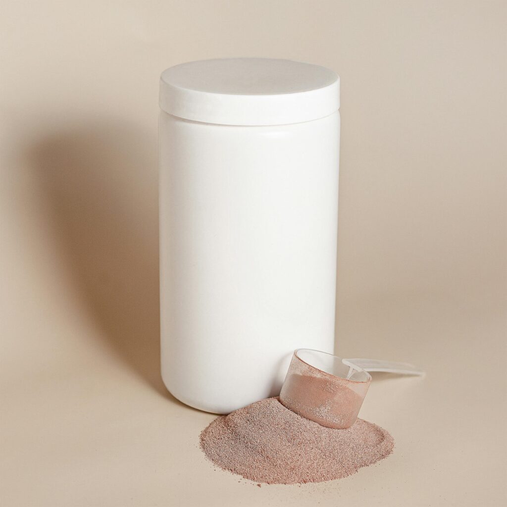 Pot de supplément blanc avec poudre de protéine brune à l'extérieur avec une cuillère à supplément au dessus de la protéine.