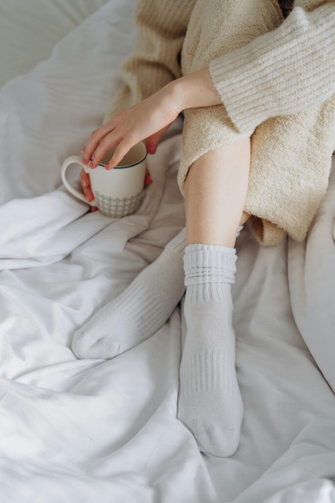 Image rapprochée sur une personne assise dans un lit tenant une tasse de café.